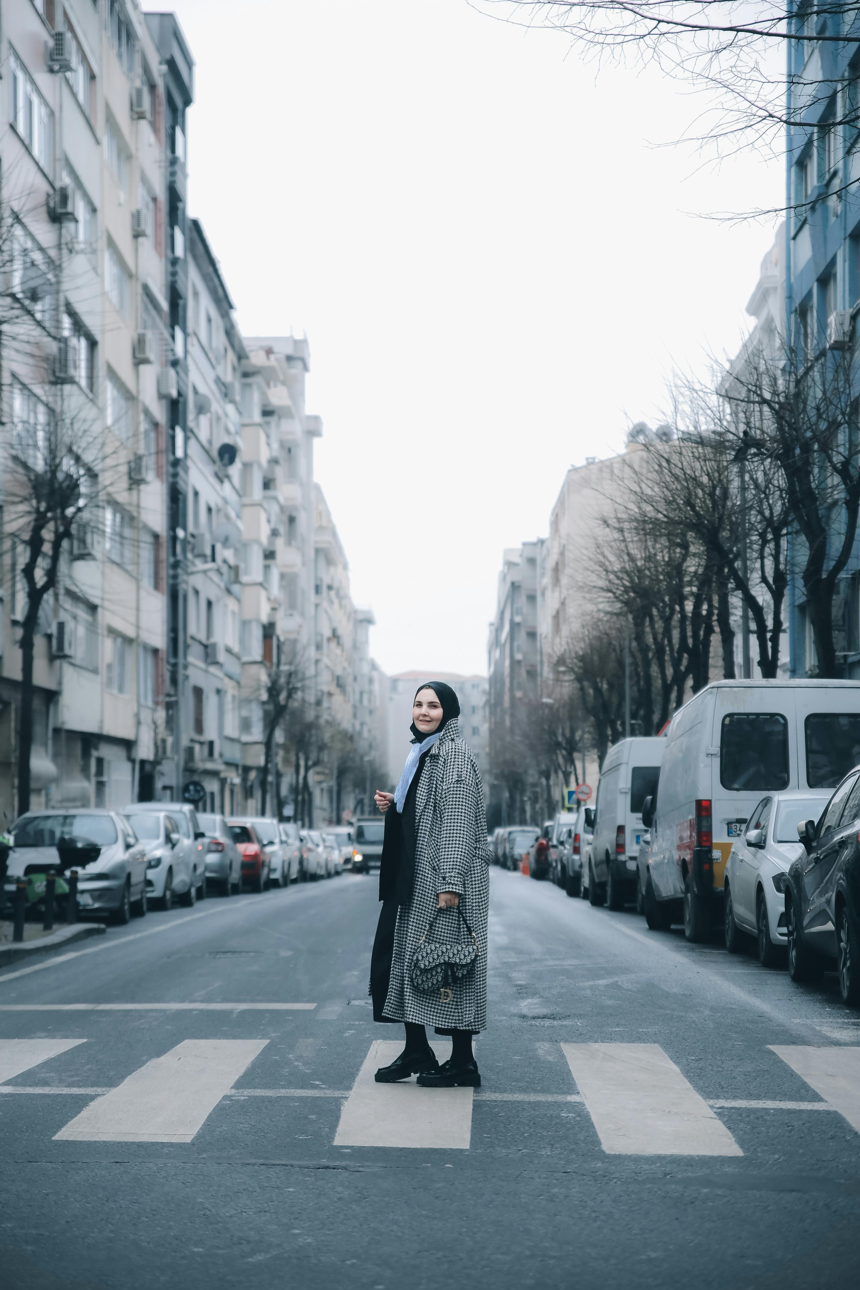 Woman in winter clothing crossing a city street on a zebra crossing, surrounded by urban buildings.