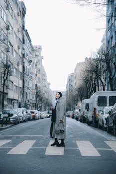Woman in winter clothing crossing a city street on a zebra crossing, surrounded by urban buildings.
