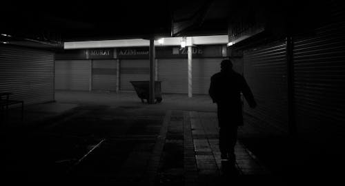 Grayscale Photo of a Person Walking on the Sidewalk