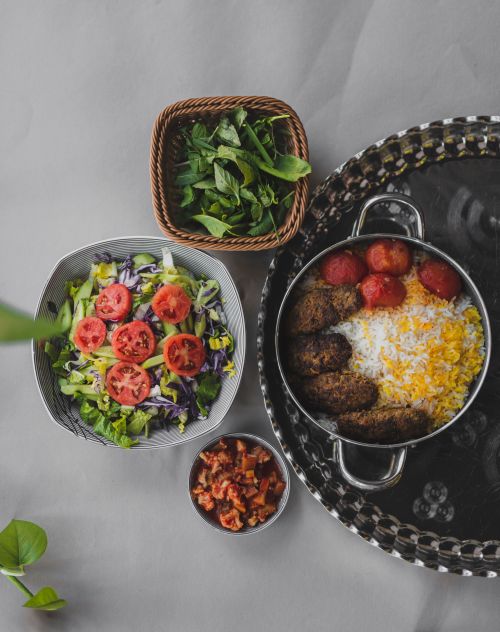 Free Overhead view of a traditional Iranian meal with koofteh, rice, salad, and fresh herbs. Stock Photo