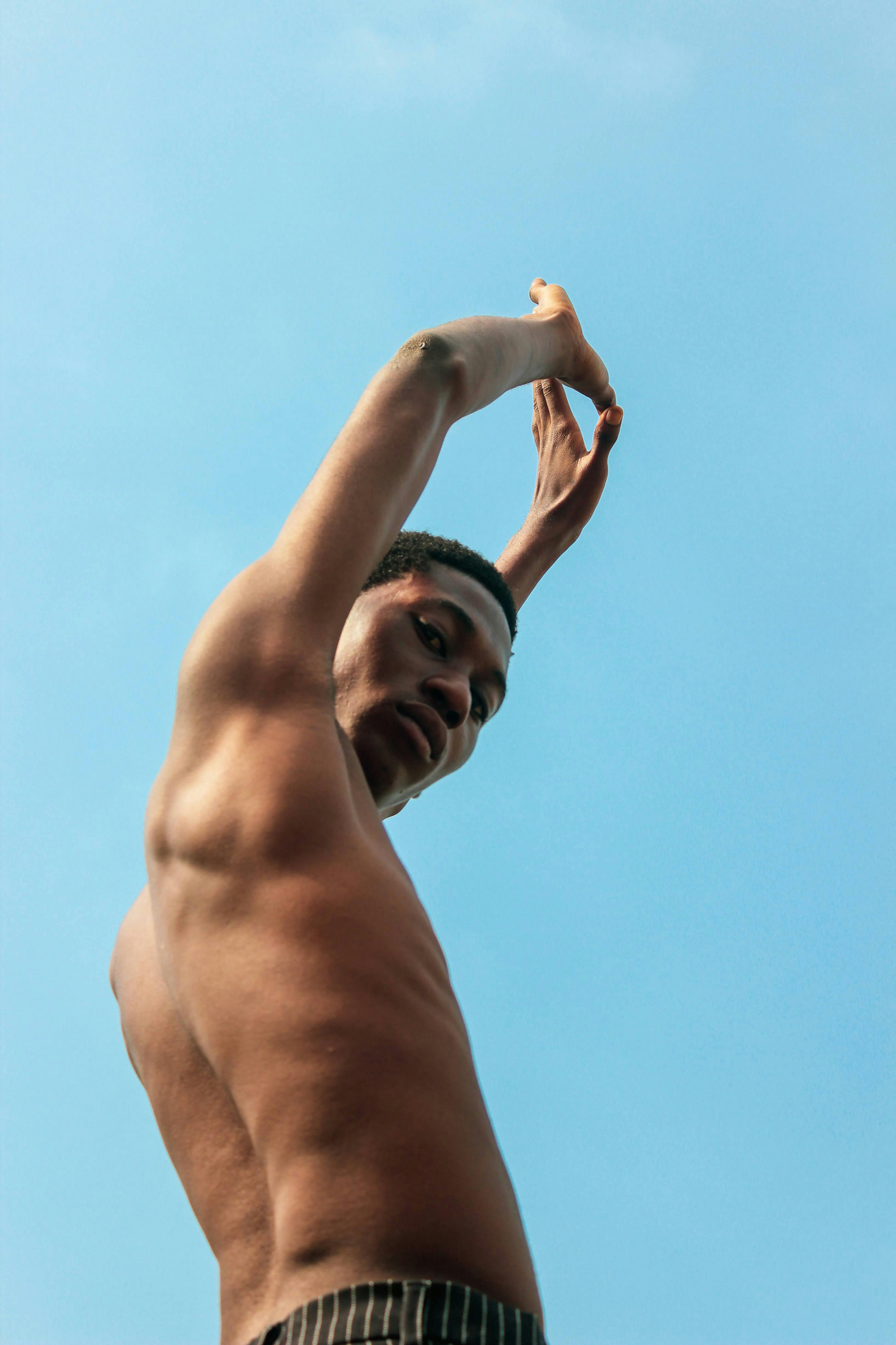 A young black man raises his arms skyward in Lagos, captured from a low angle on a clear day.