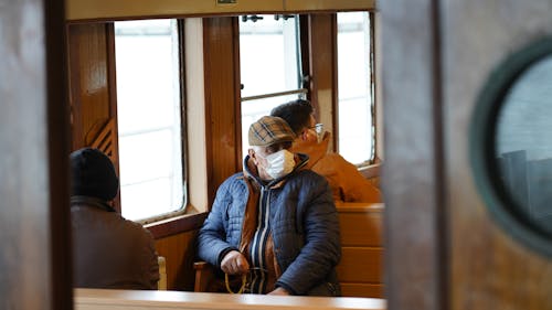 Man in Blue Jacket Wearing White Face Mask Sitting on Wooden Chair