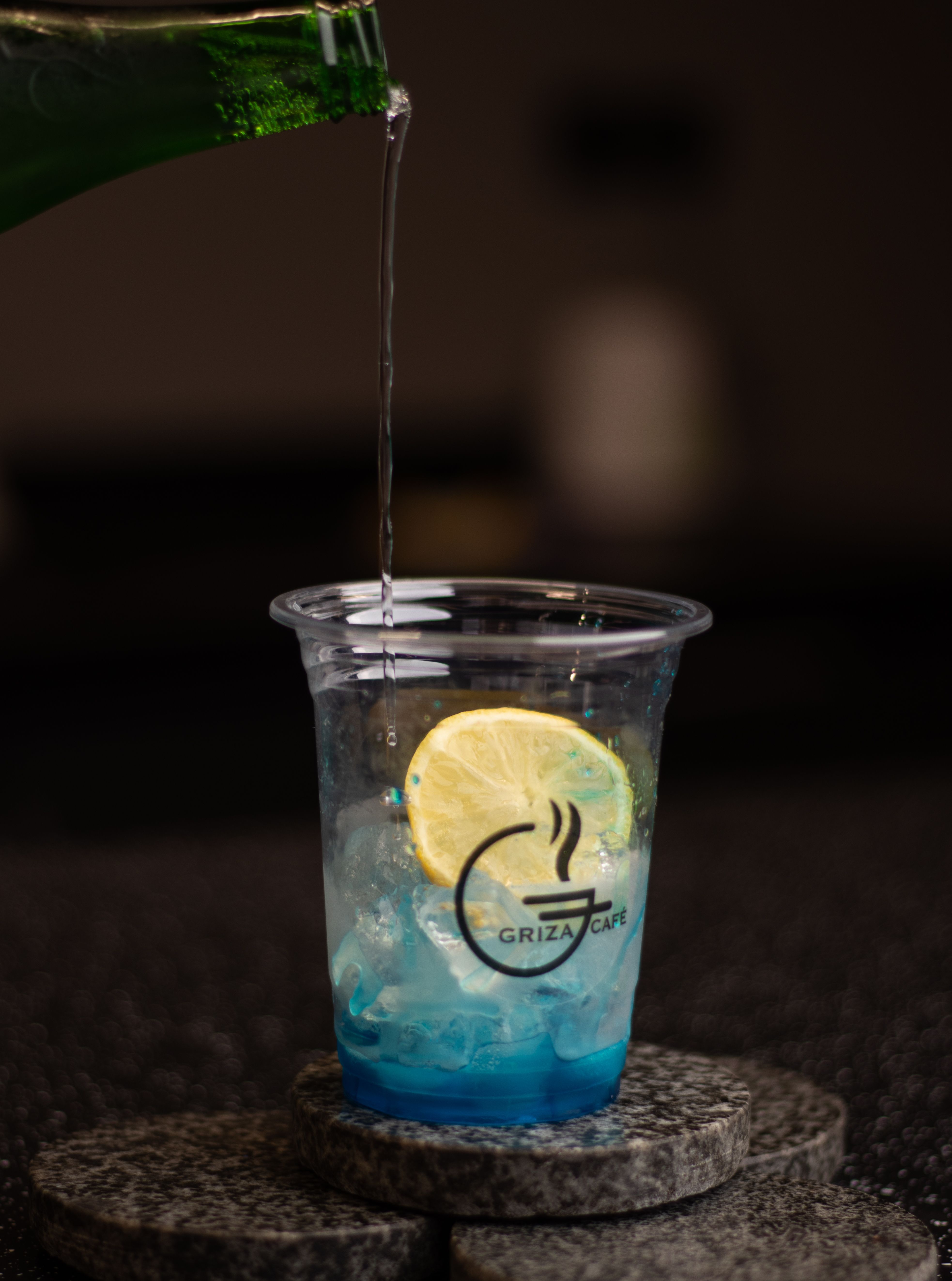 Pouring a cold beverage into a disposable cup with ice and lemon slice.