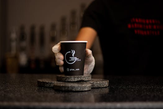Close-up of a barista's hand holding a steaming coffee cup at Griza Cafe.