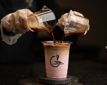 Close-up of a barista pouring espresso into a chilled coffee drink at Griza Cafe.