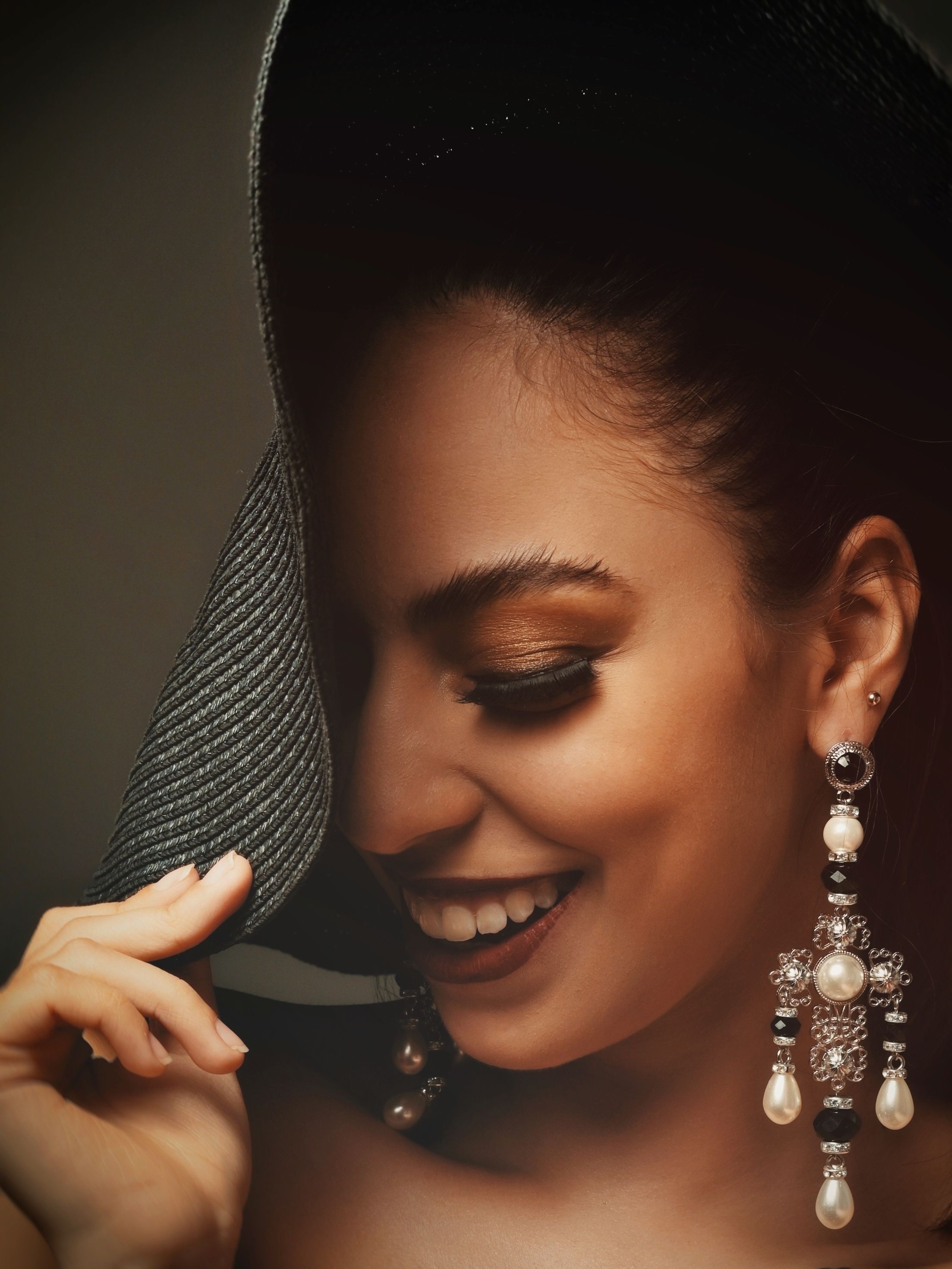 Close-up de uma mulher sorridente usando um chapéu e brincos elegantes.