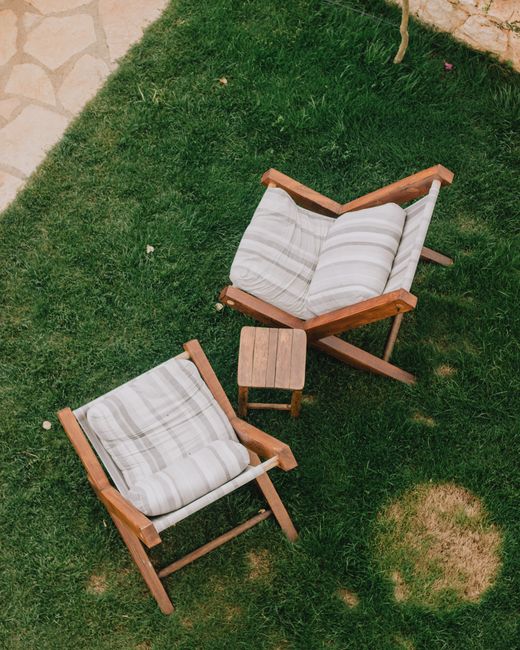 Overhead shot of wooden chairs with cushions and table on a grass lawn, perfect for outdoor relaxation.