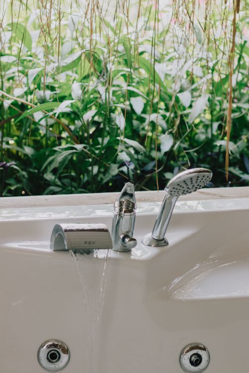 Free Stylish ceramic bathtub with a modern faucet and showerhead facing a lush green garden. Stock Photo
