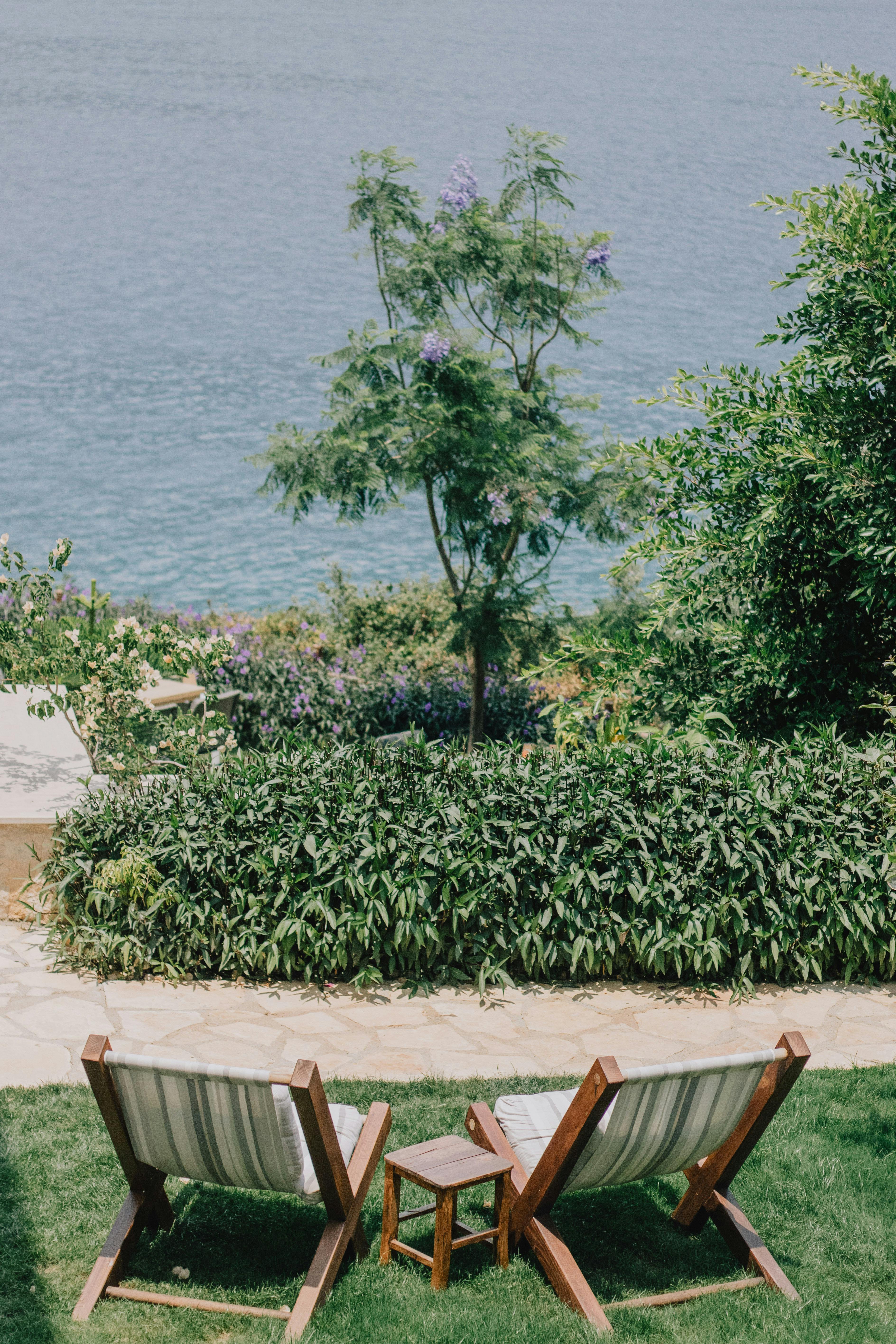 A tranquil seaside garden scene featuring two lounge chairs facing the ocean, surrounded by greenery.