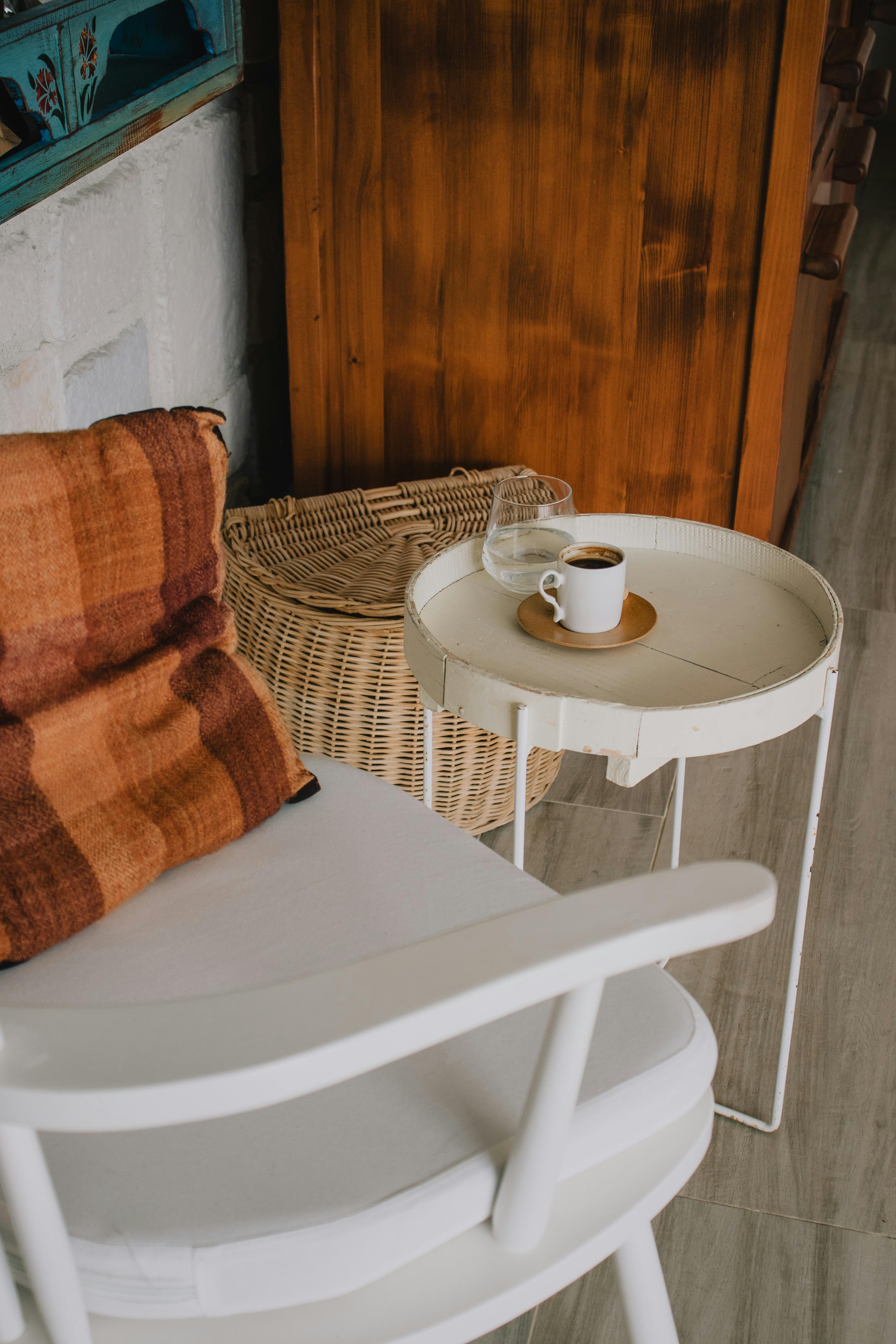 Free Stylish cozy corner featuring a white chair, small table, and coffee cup for relaxation. Stock Photo