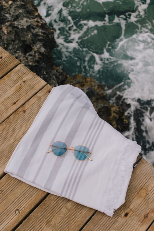 Free Sunglasses and towel on a wooden deck by the sea, perfect for summer vibes. Stock Photo
