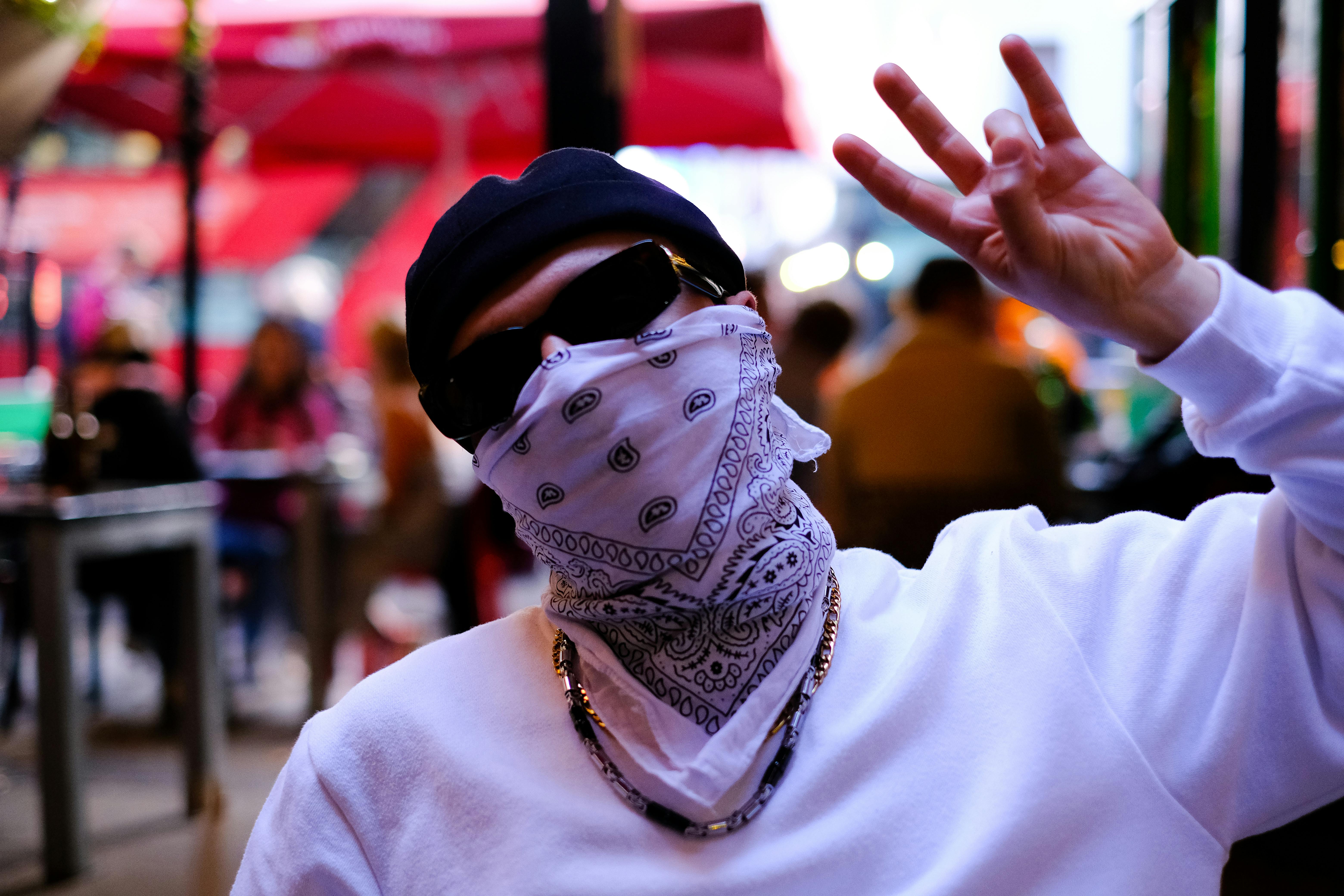 Man wears a blue bandana, black sunglasses, white face mask, brown