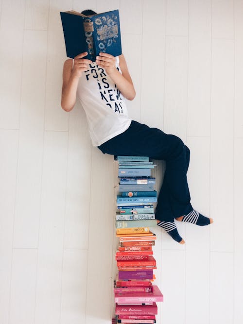 A Person Sitting on a Stack of Books and Reading 