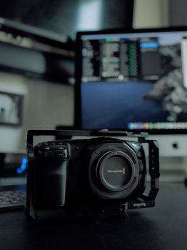 Close-up of a professional camera in a metal frame on a desk with a computer screen in the background.