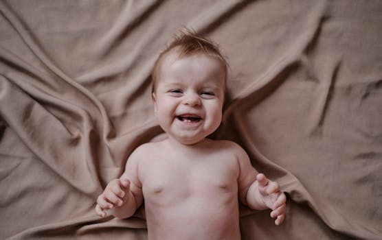 A happy baby laughing while lying on a soft, neutral-colored fabric, capturing pure joy.