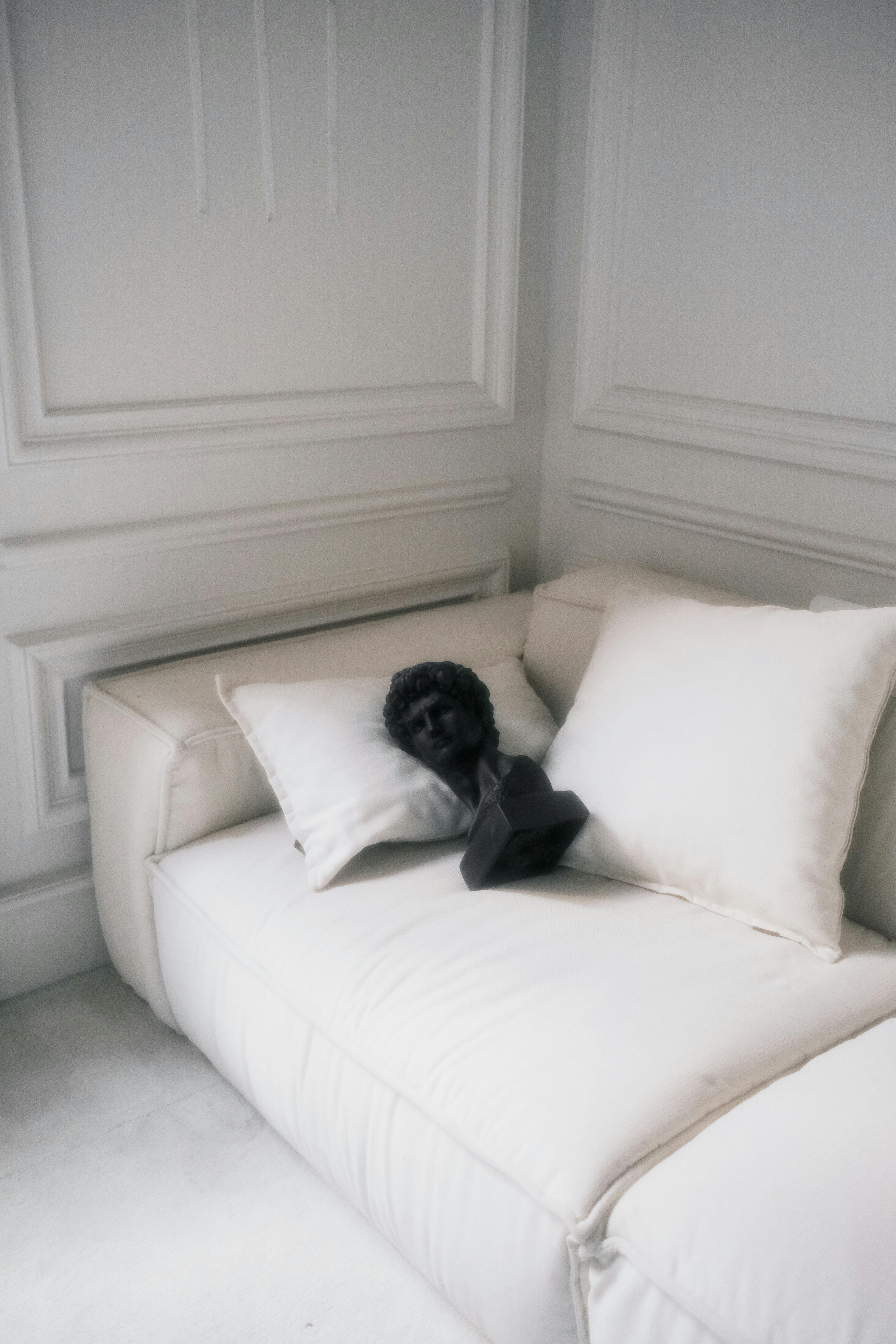 Free A black bust sculpture placed on a white couch in a stylish living room setting. Stock Photo
