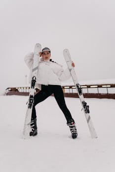 Stylish woman in sports attire poses confidently with skis in snowy landscape.