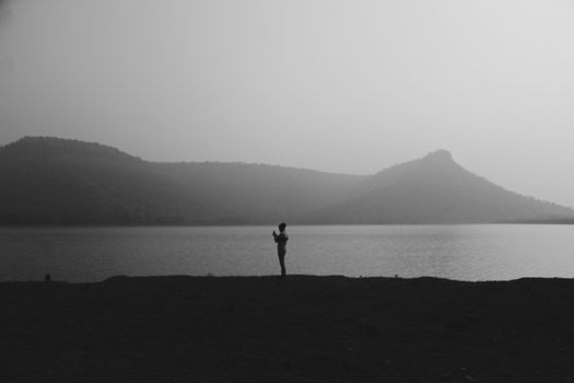 A lone figure silhouetted against a misty lake and distant mountains at twilight, conveying solitude.