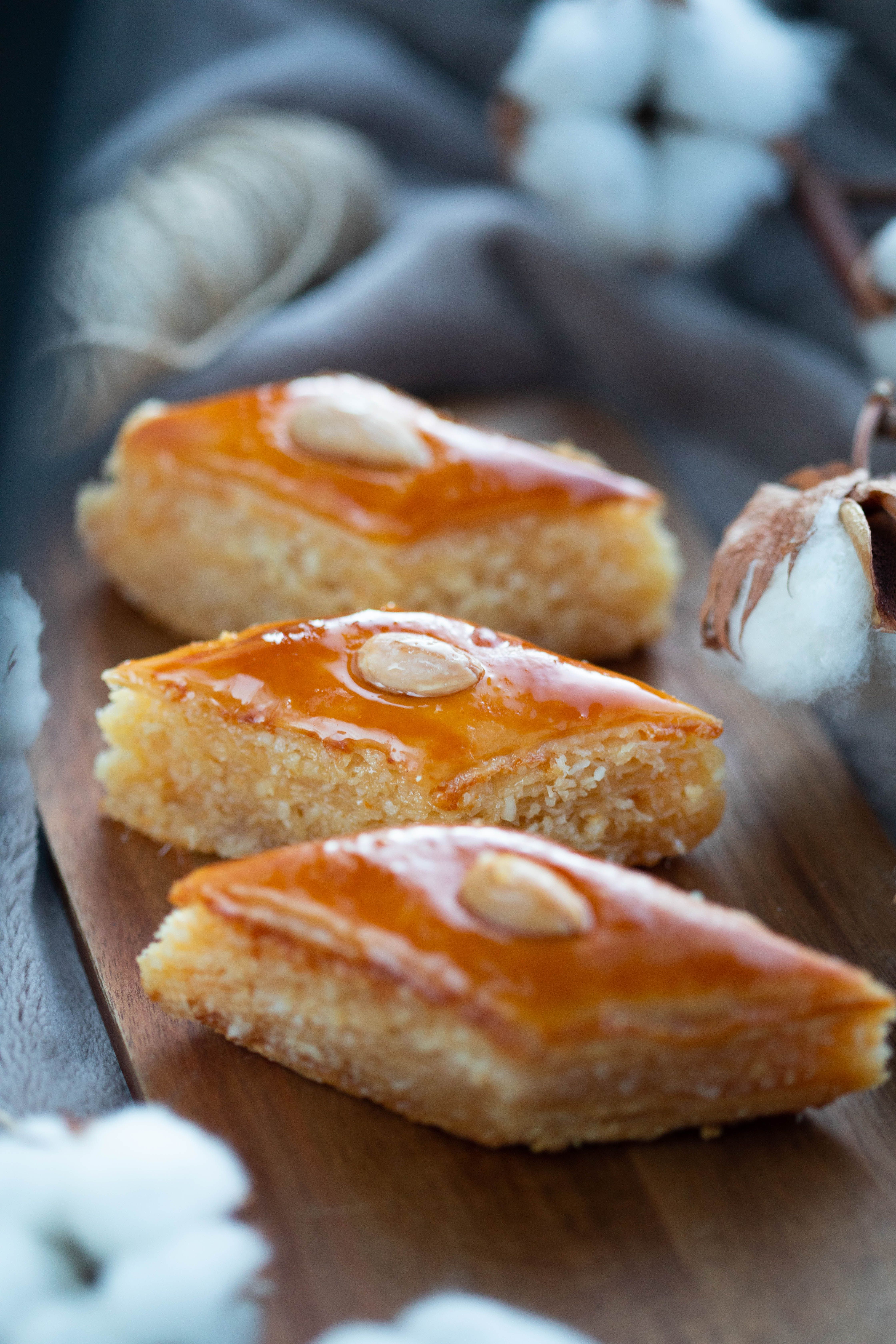 Close-up of sweet, honey-soaked diamond pastries with almonds on a wooden board.