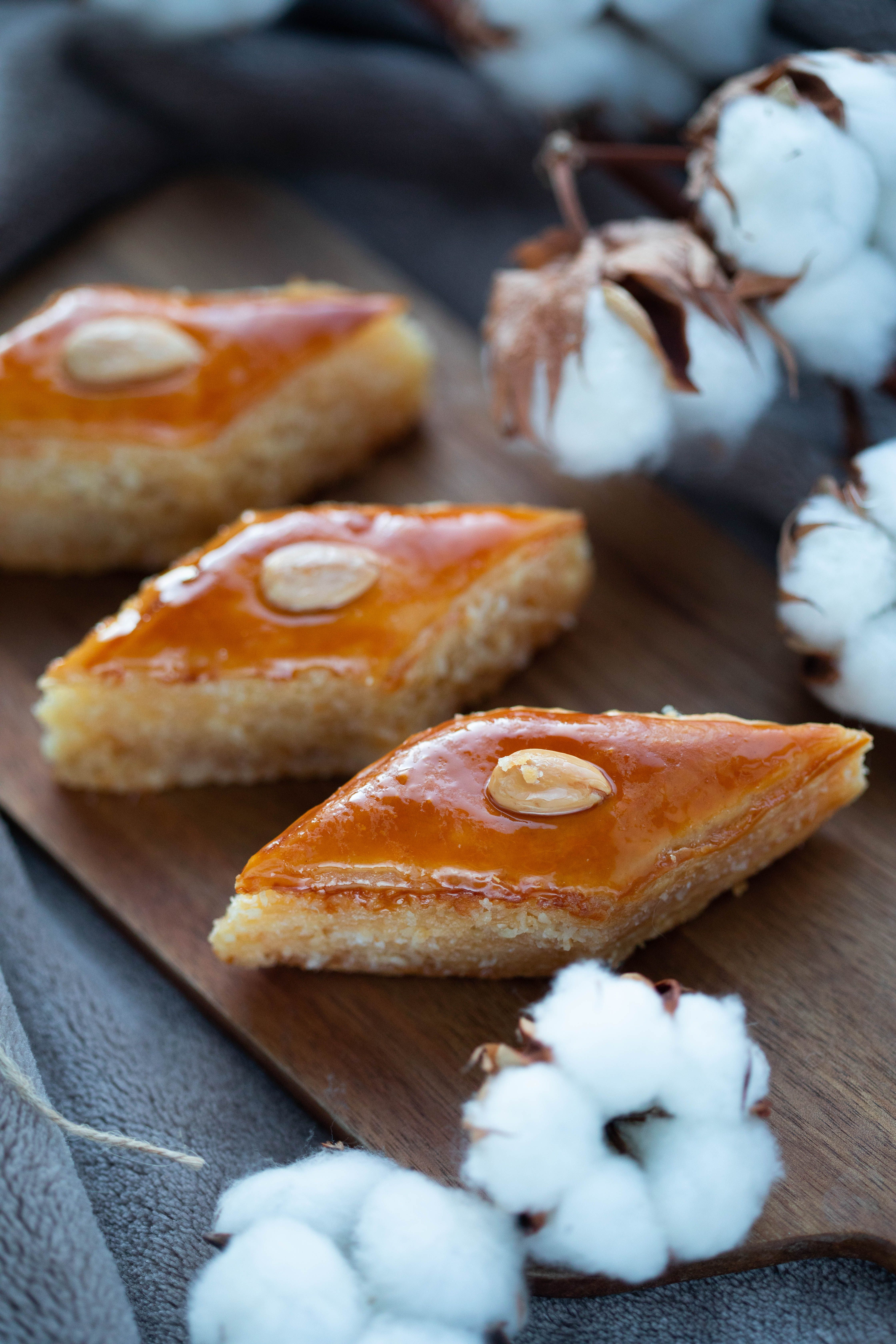 Close-up of golden almond baklava pieces on a rustic wooden board with cotton for decoration.