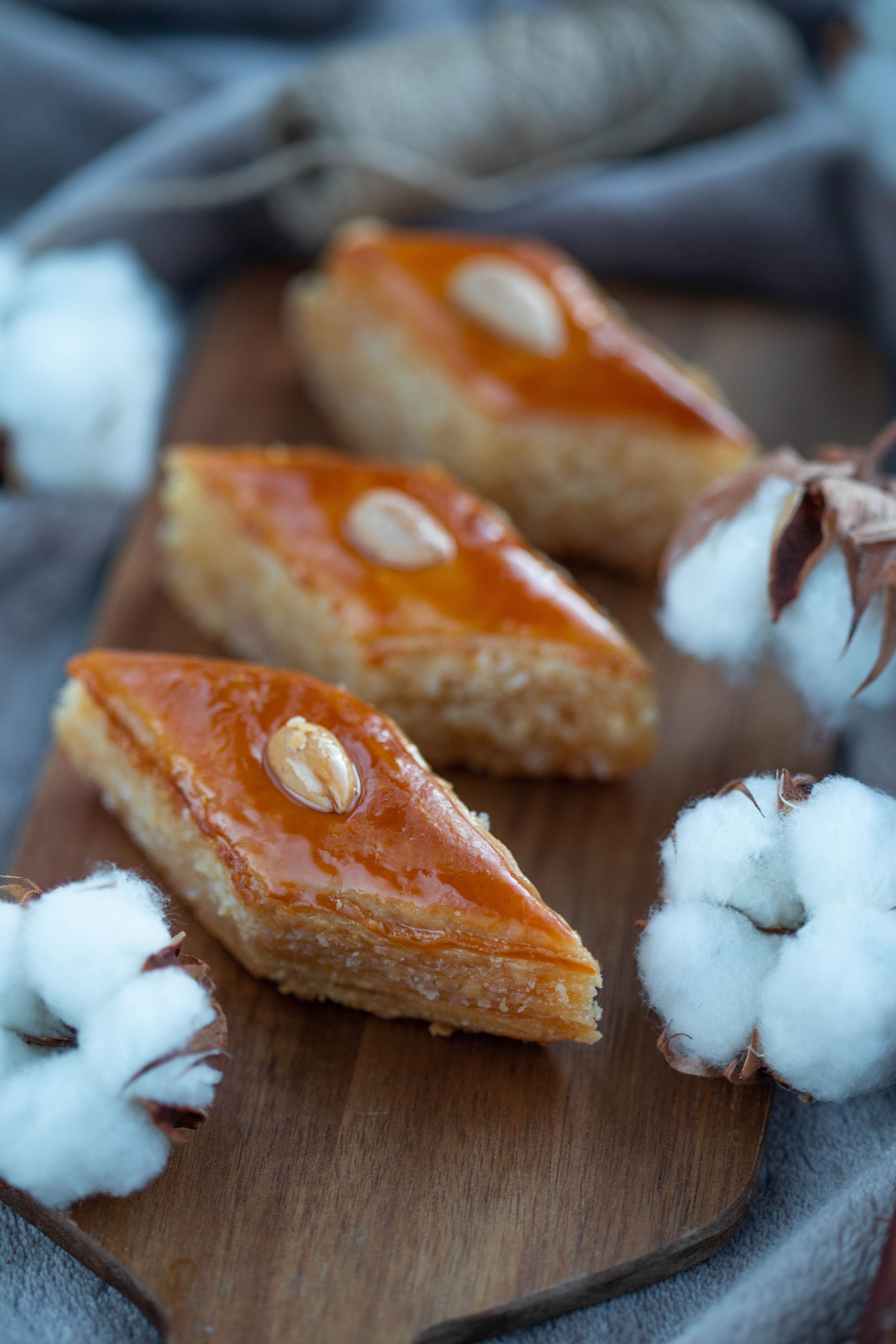 Close-up of sweet baklava slices on a wooden board with cotton flowers, highlighting their tasty appearance.