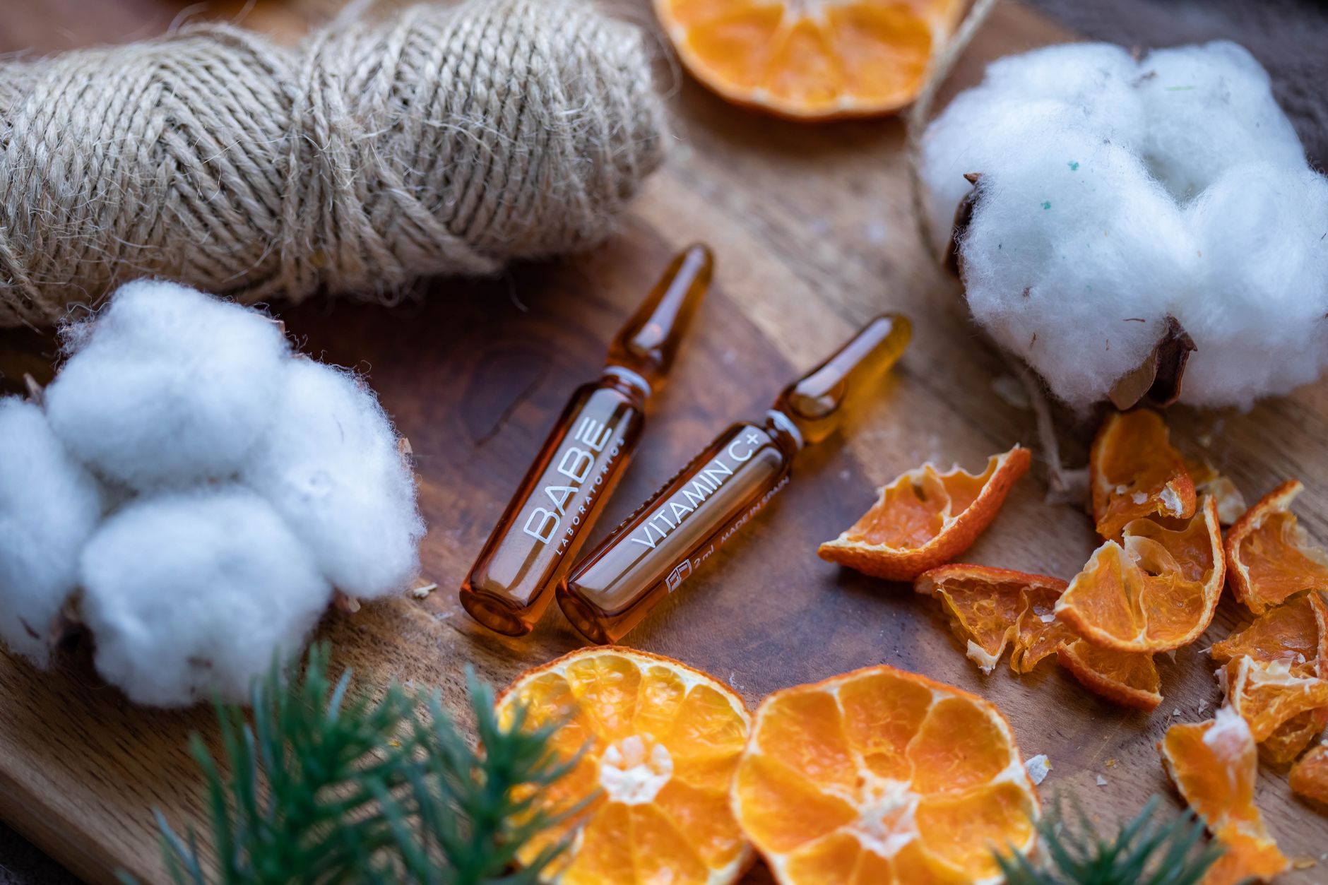 Close-up of skincare ampoules with dried citrus, cotton, and twine, exuding a natural healing vibe.