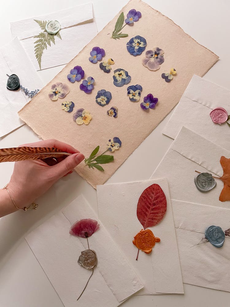 Hand Holding Feather Over Decorated Sheet And Envelopes