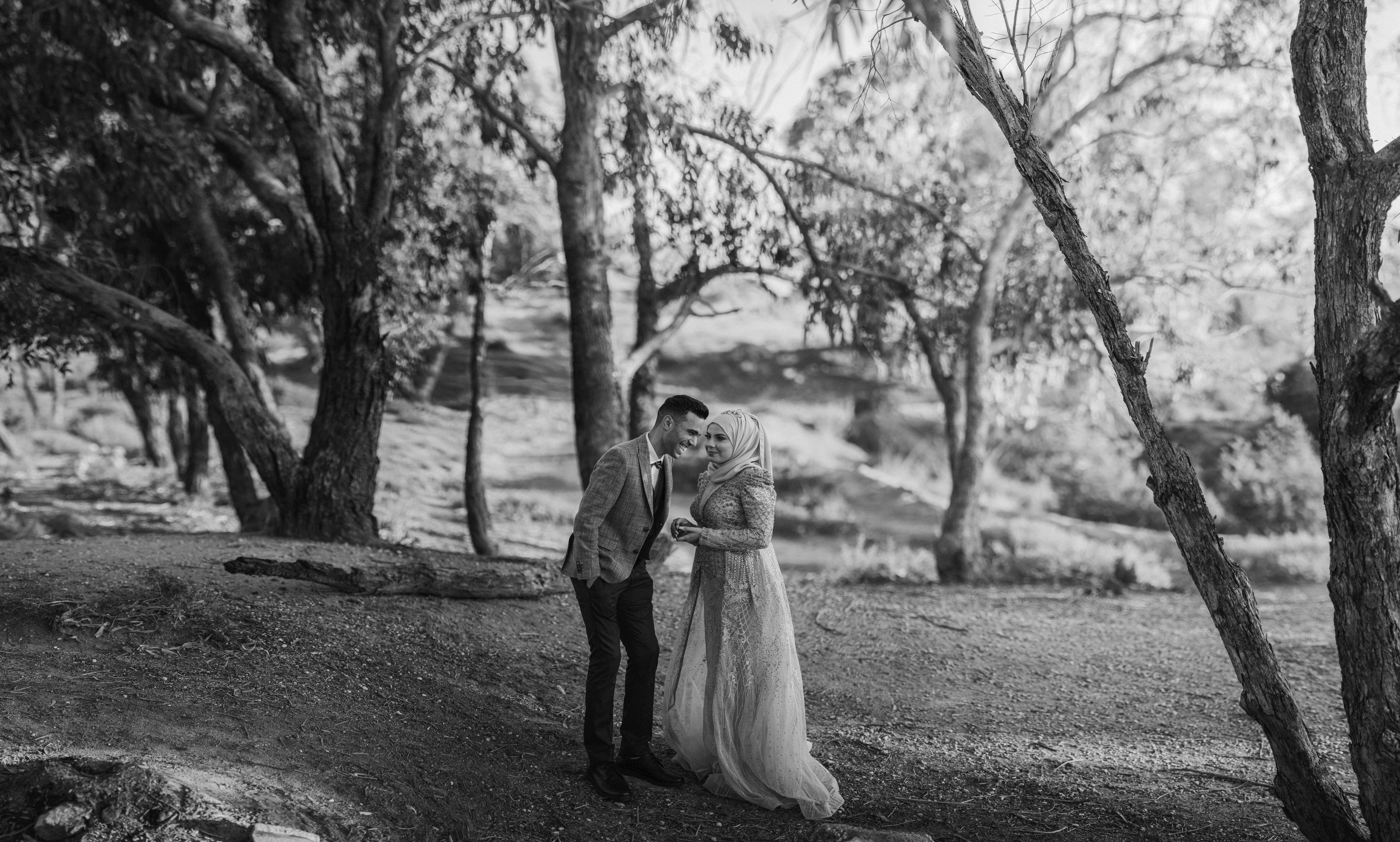 A candid black and white wedding photo of a couple embracing outdoors.