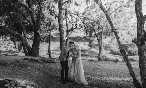 Grayscale Photo of a Groom and a Bride Near Trees