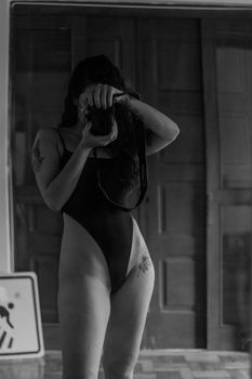 A woman captures a self-portrait using a camera, emphasizing artistic tones in a black and white swimsuit shot.