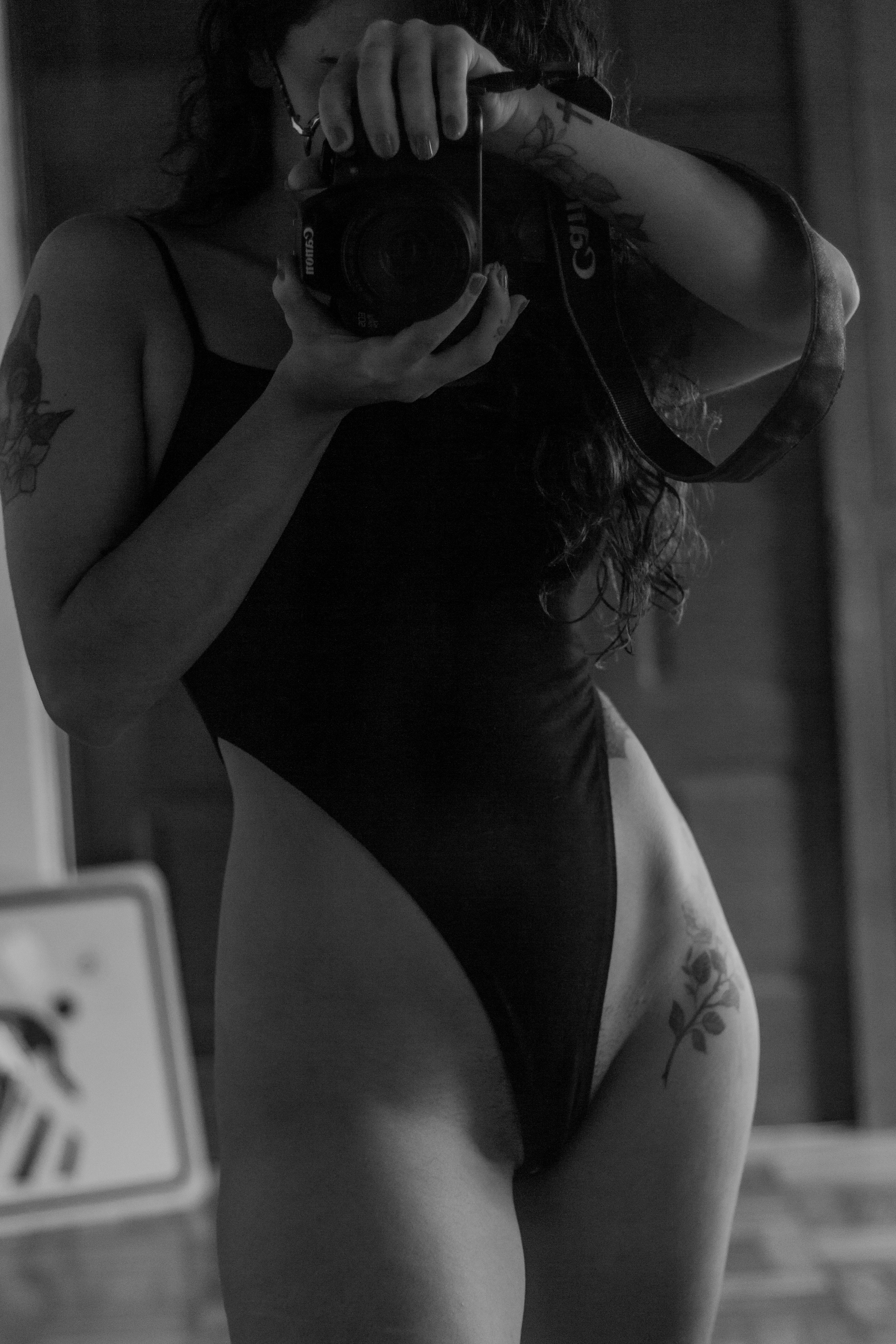 Close-up black and white portrait of a woman photographer in swimwear holding a camera.