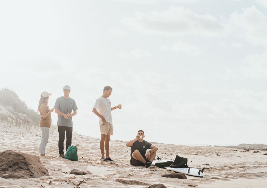 Group of friends relaxing on a beach, drinking and chatting in a sunny setting.