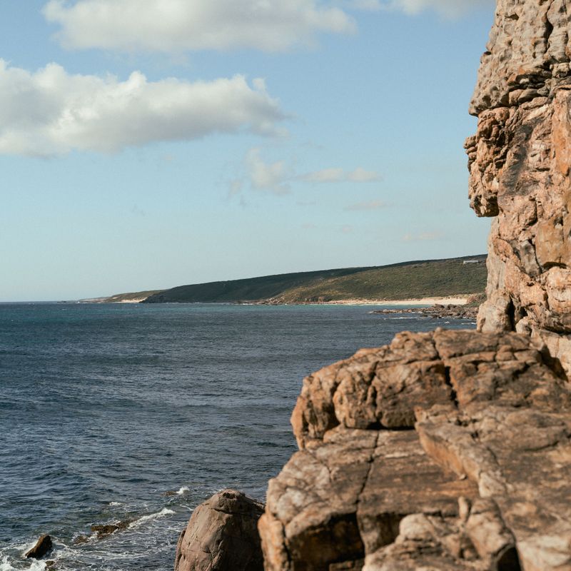 Rugged sandstone cliffs above a calm sea under a pale blue sky