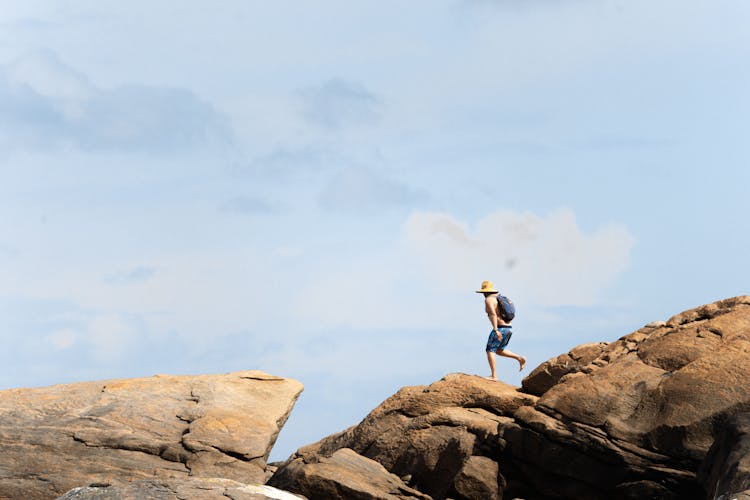 Person Wearing Hat And Backpack Walking On Rocks