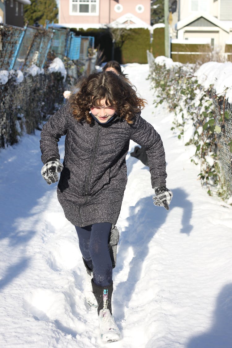 Girl Wearing A Jacket Running On Snow Covered Walkway