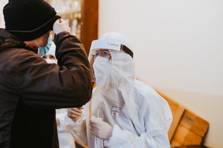 Healthcare Worker Wearing Protective Suit And A Mask Looking At Patient 