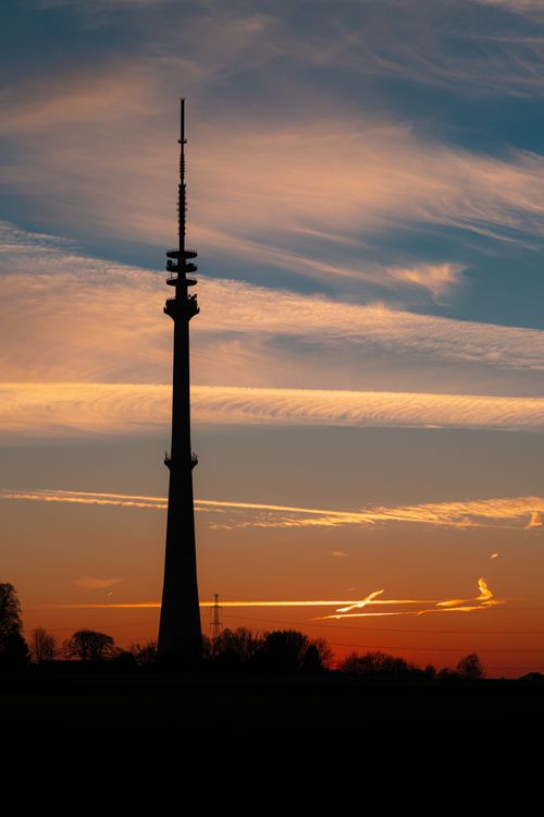 Free Silhouette of a tall radio tower against a vibrant sunset sky in Sint-Pieters-Leeuw, Belgium. Stock Photo