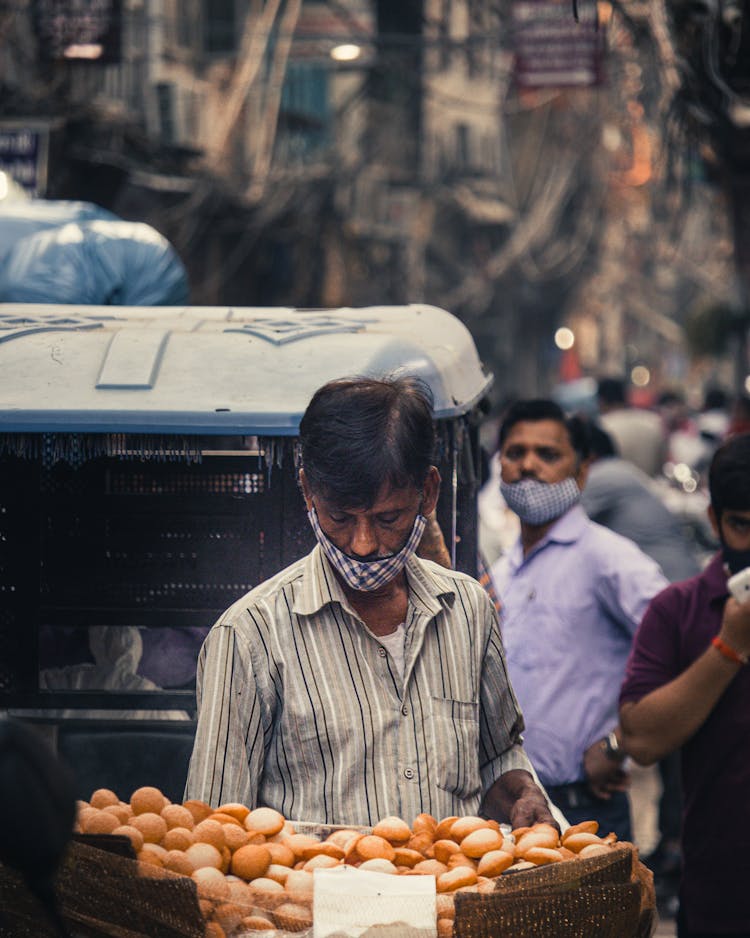 Man Standing In Front Of A Basket Full Of Bread In Busy Marketplace