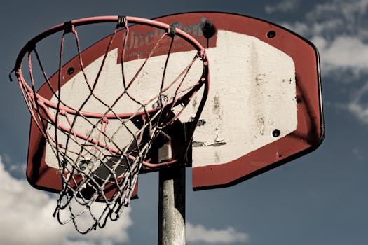 Rustic basketball hoop with worn backboard and net against a cloudy sky.