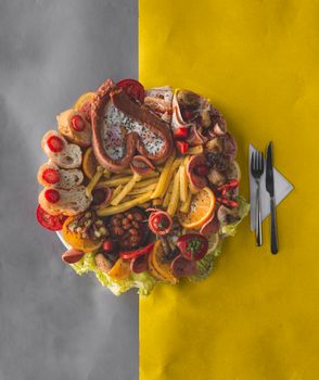 Vibrant arrangement of assorted foods on plate with cutlery on yellow and gray surface.