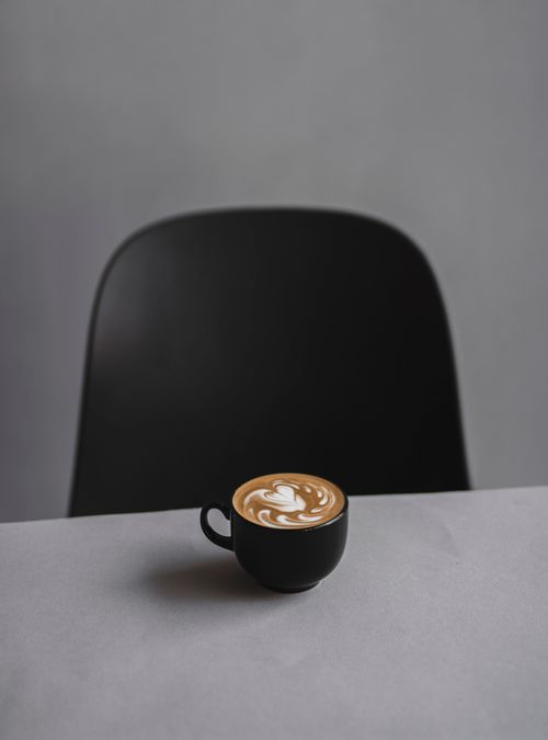Free A minimalist coffee scene featuring a latte with art, black chair, and simple backdrop. Stock Photo
