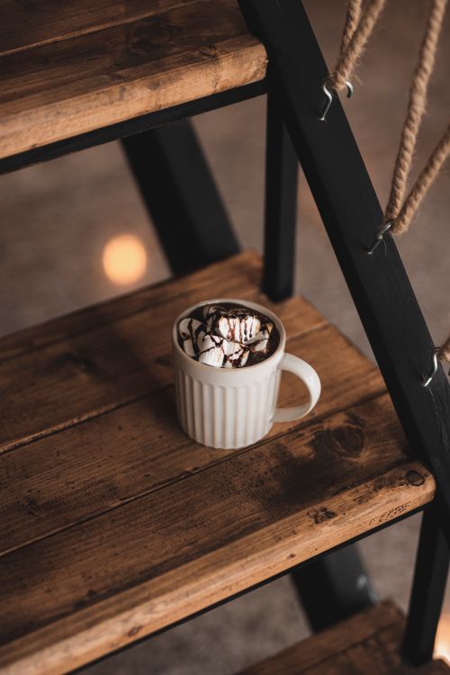 Free Warm cup of hot chocolate with marshmallows set on rustic wooden stairs, evoking cozy winter vibes. Stock Photo