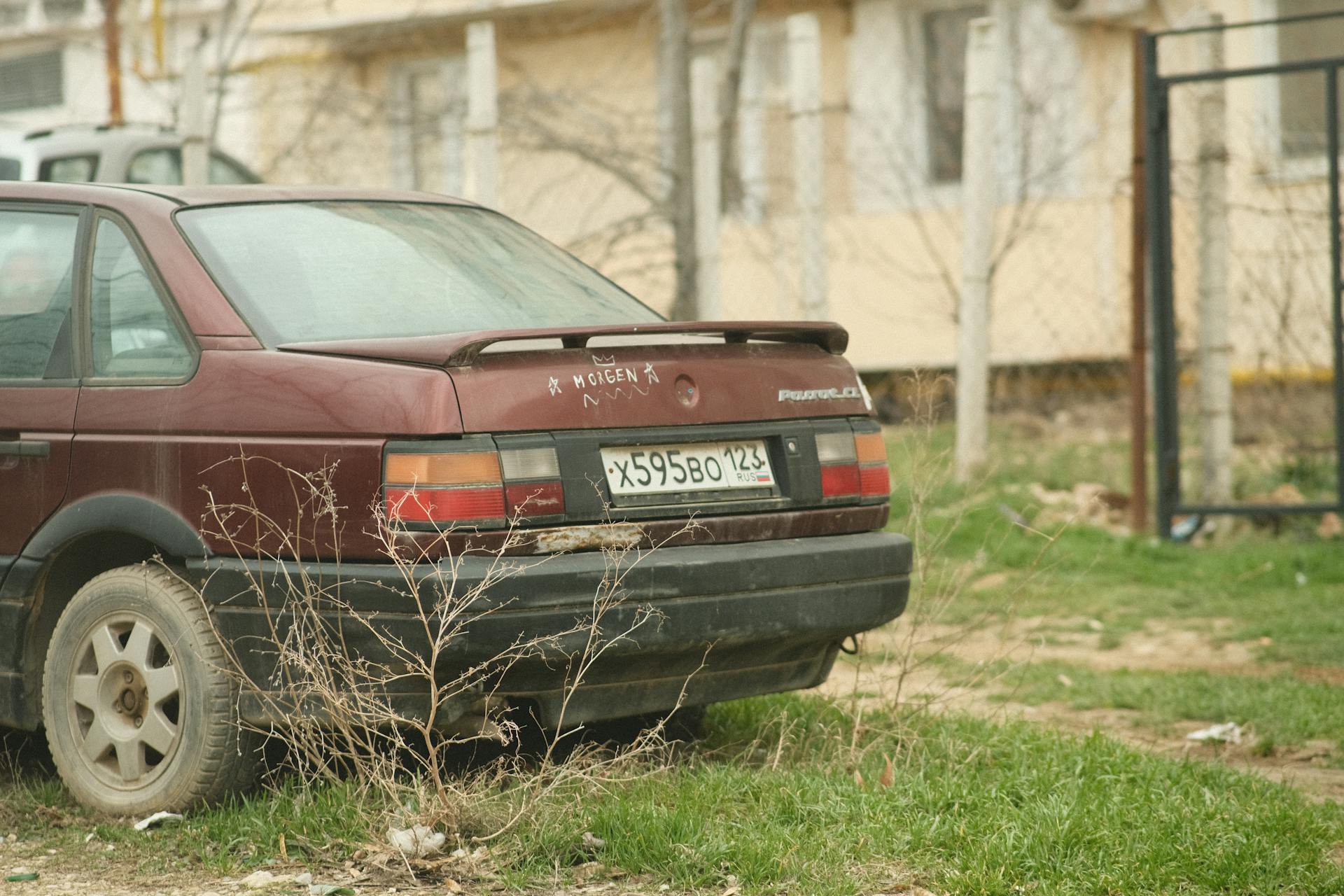 An old vintage car parked in a residential area with a focus on the trunk and license plate.