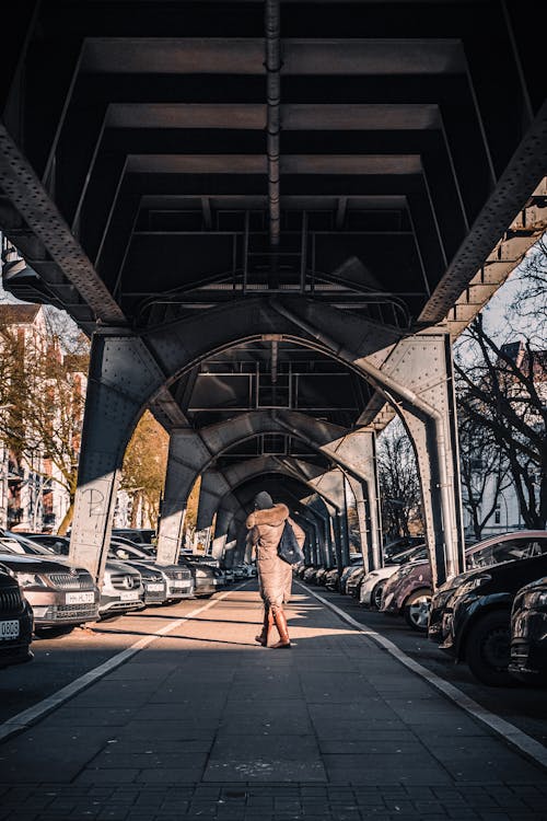 Woman in Black Tank Top and Blue Denim Jeans Standing on Sidewalk Under Bridge