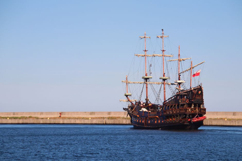 A classic pirate ship sailing along a peaceful harbor under clear blue skies.