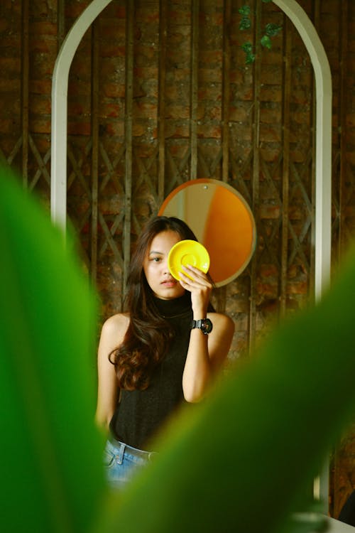 Woman Holding Yellow Plate to Cover Her Eye 