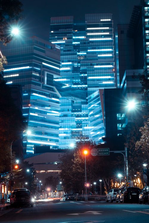Free Stunning night view of illuminated modern glass buildings with parked cars on the vibrant city street. Stock Photo