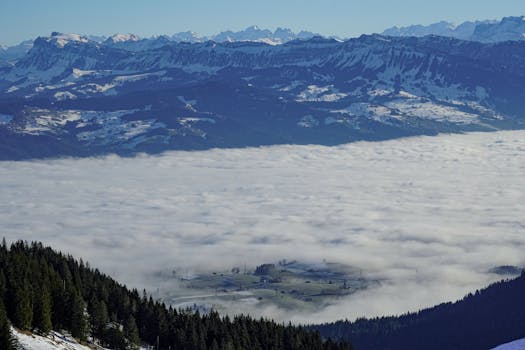 Stunning view of fog rolling over the valley surrounded by snowcapped mountains in Rüeggisberg, Switzerland.