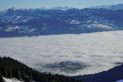 Free Stunning view of fog rolling over the valley surrounded by snowcapped mountains in Rüeggisberg, Switzerland. Stock Photo