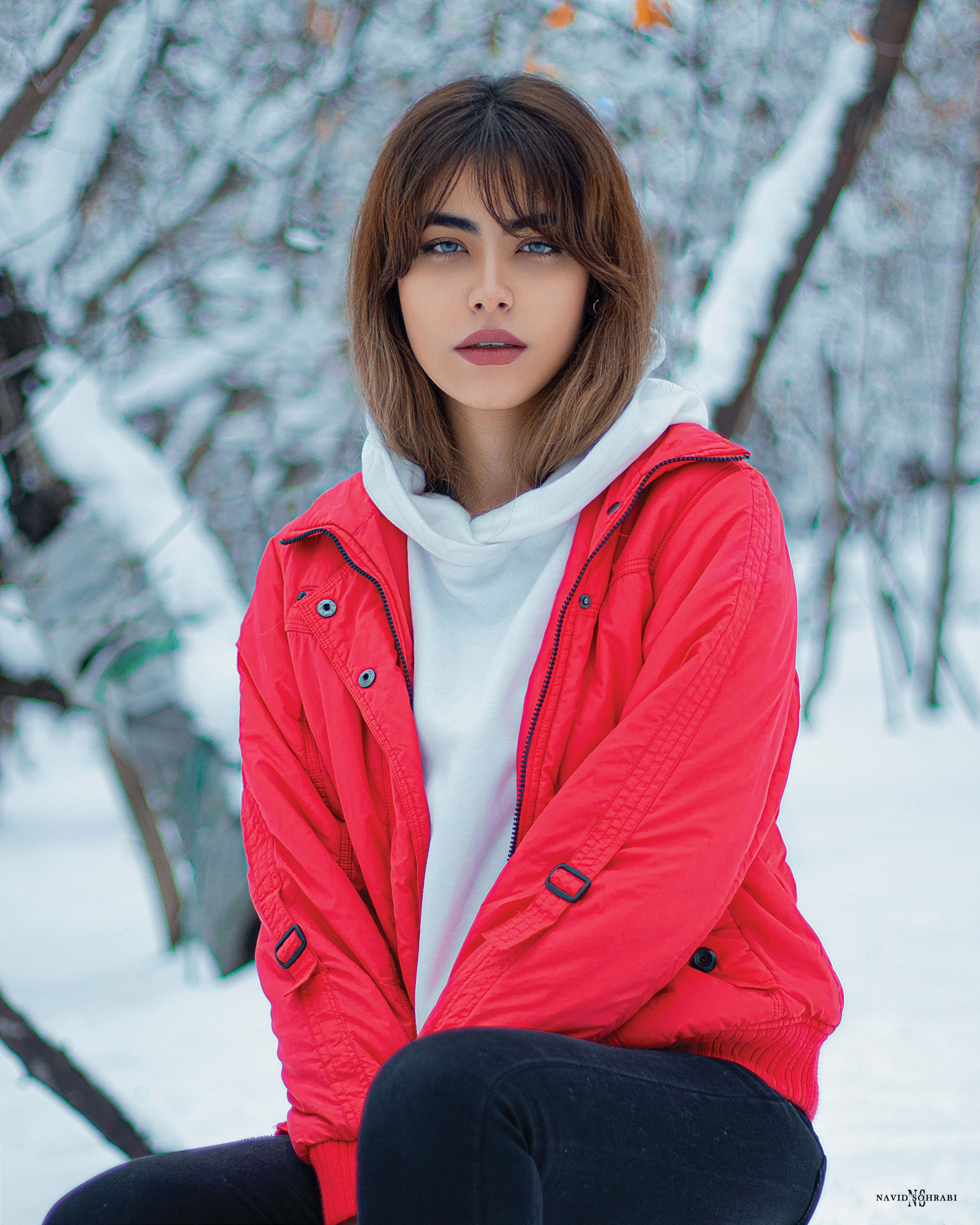Portrait of a woman in a red jacket sitting in a snowy forest, exuding warmth and elegance.